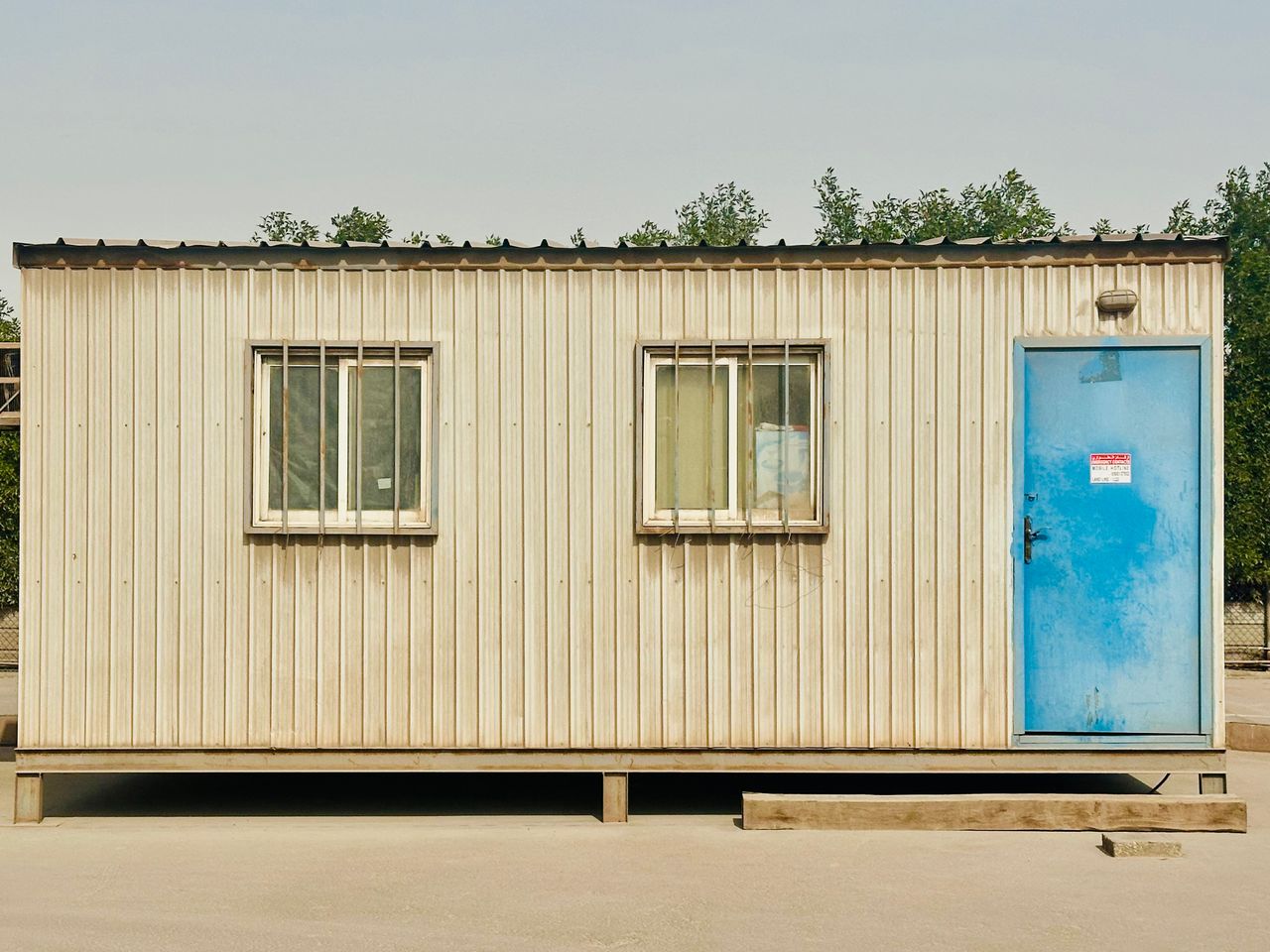 A portable cabin with a distinctive blue door in a sunny outdoor setting in Saudi Arabia.